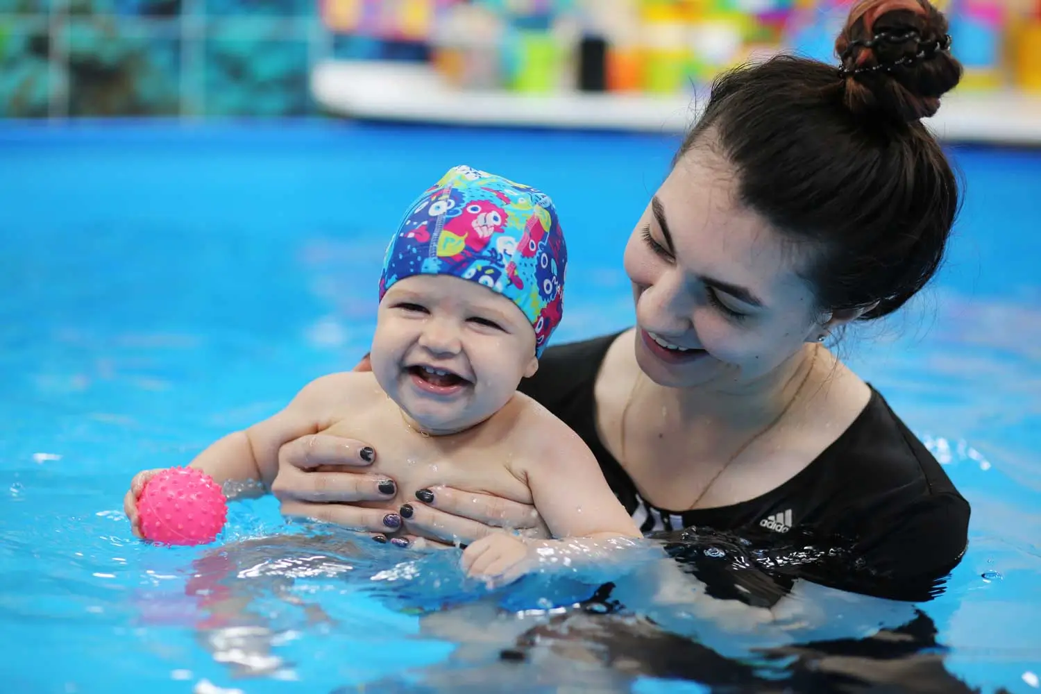 Мама стоит в бассейне и держит руками малыша
