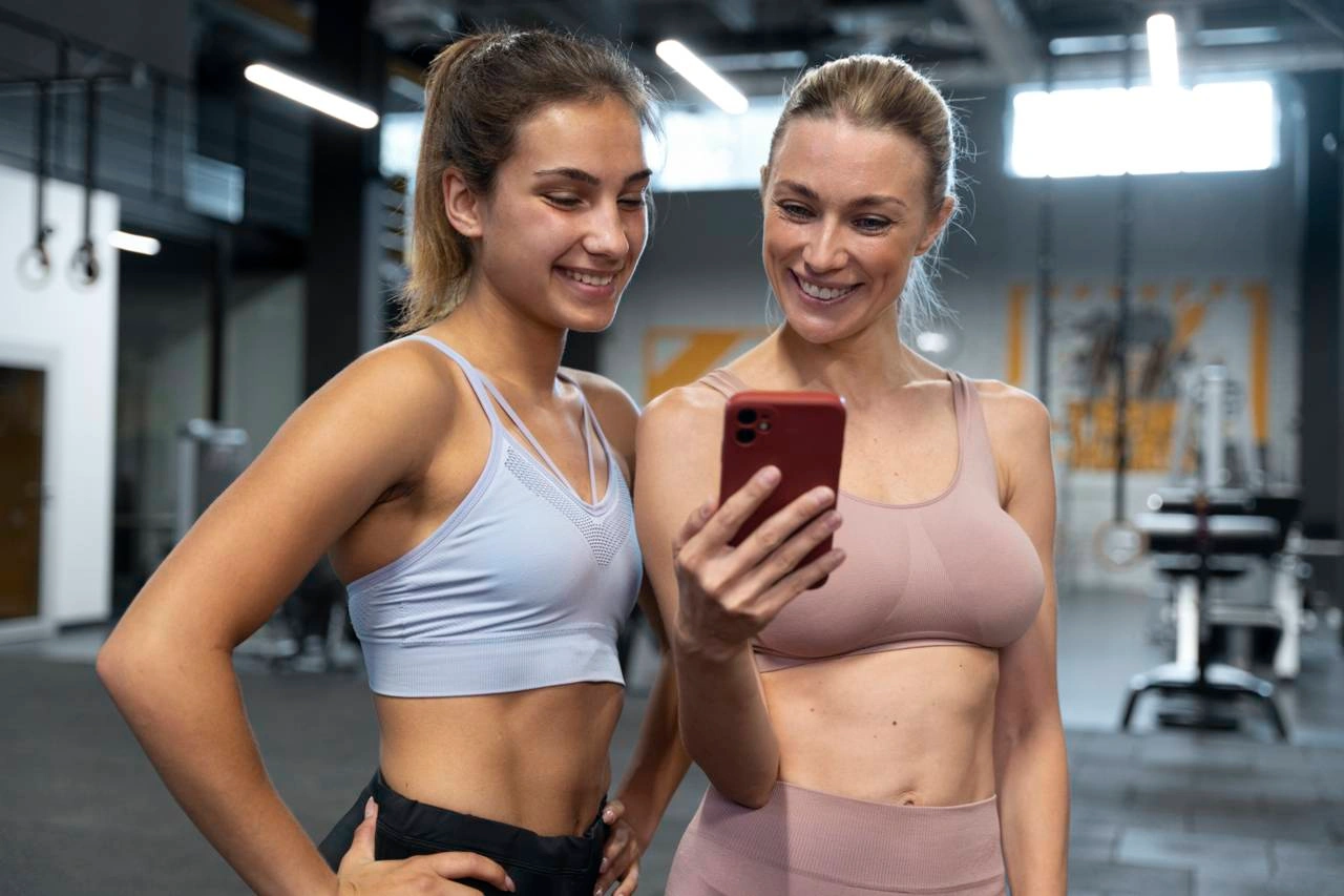 Две спортсменки вместе смотрят в смартфон и улыбаются