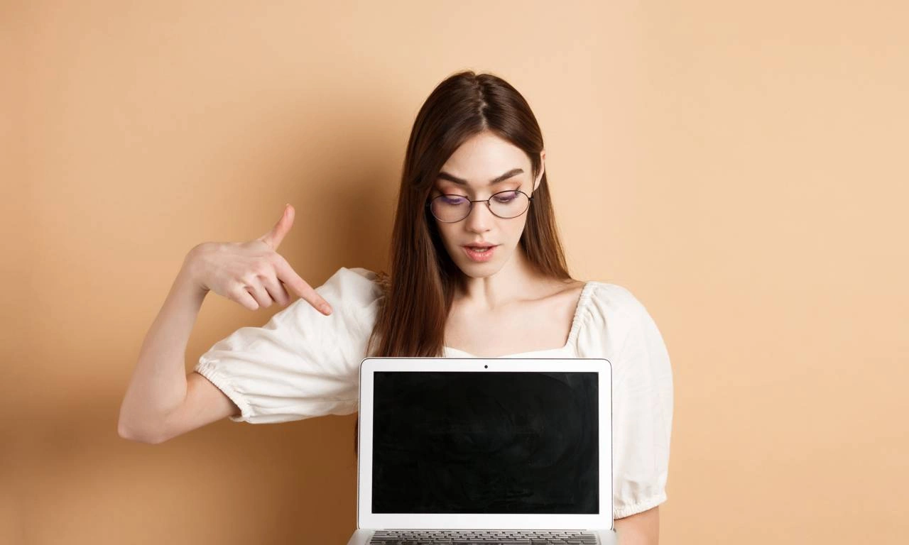 Девушка в очках указывает пальцем на ноутбук