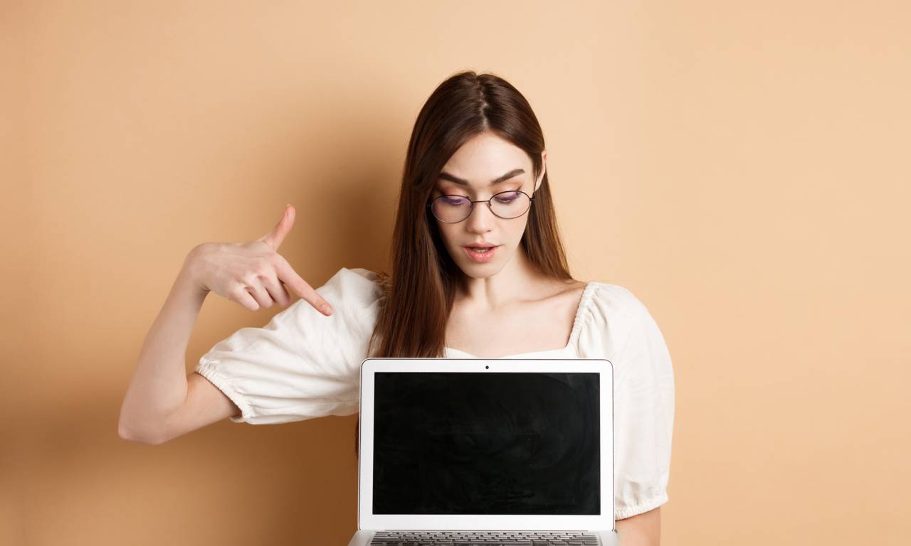 Девушка в очках указывает пальцем на ноутбук