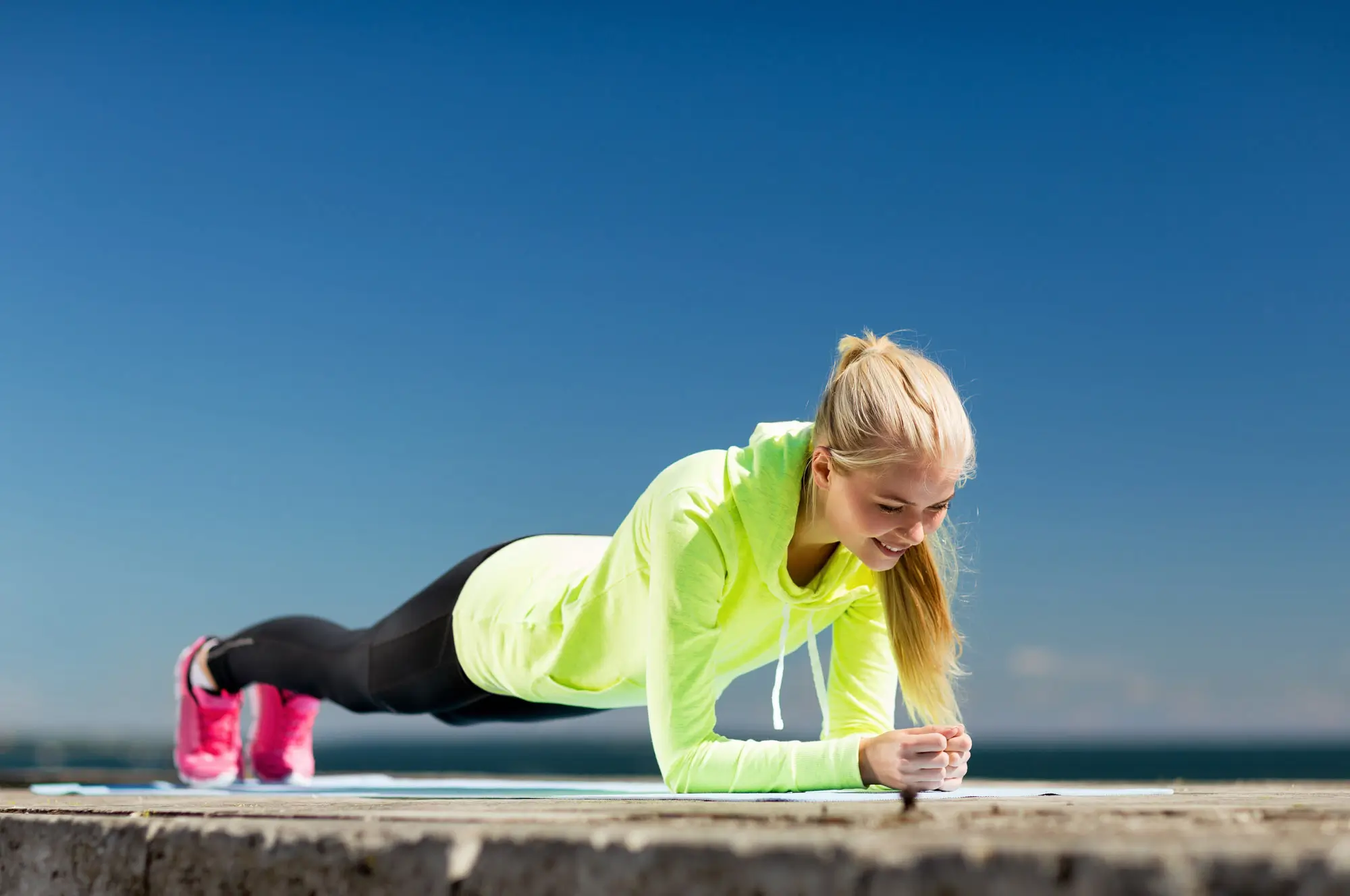 Девушка стоит в планке и широко улыбается